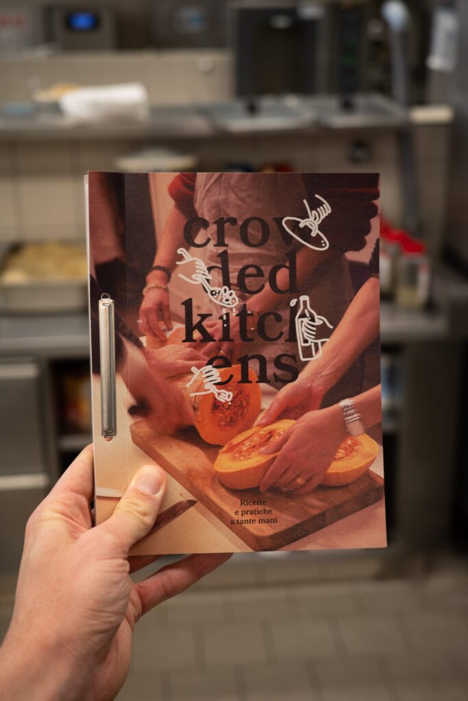 Hand holding a small booklet with the title "crowded kitchens"